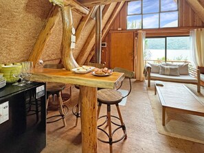 A rustic wooden interior with a dining area, bar stools, and a sofa with cushions.