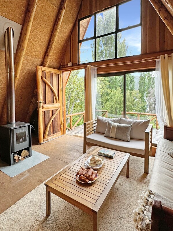 A cozy room with a wooden ceiling, a sofa, a table with bread, and a wood-burning stove.