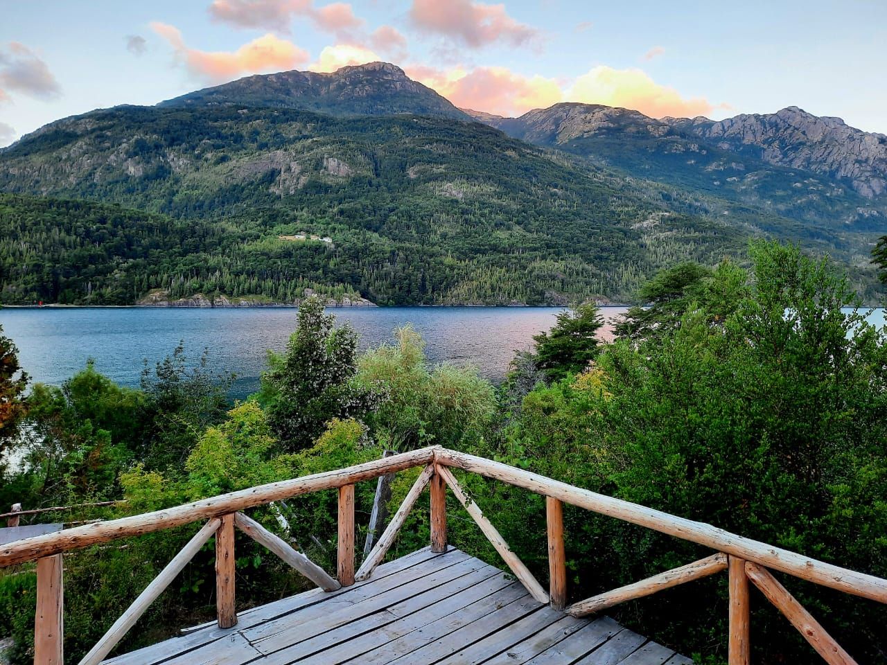 Une terrasse en bois avec une rambarde donnant sur un lac et des montagnes.