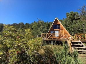 Una cabaña de madera con balcón, rodeada de follaje denso.