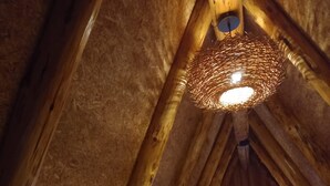 Una habitación con techos altos y un techo de madera inclinado, una cama con ropa blanca y una lámpara de fibra.