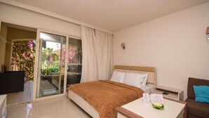 Ein Hotelzimmer mit Bett, Schreibtisch, Stuhl, Nachttisch und einer Glastür zum Balkon mit Blumen.