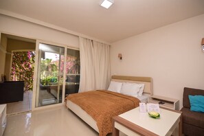 Una camera d'albergo con un letto, una scrivania, una sedia, un comodino e una porta scorrevole in vetro che dà su un balcone fiorito.