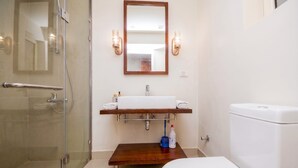 Ein Badezimmer mit einer Duschkabine aus Glas, einer weißen Toilette, einem Holzbadezimmermöbel mit Waschbecken und zwei Wandleuchten.