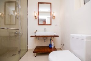 Un bagno con box doccia in vetro, un water bianco, un mobile bagno in legno con lavabo e due applique.