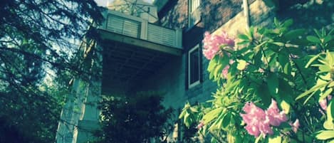 Ein Gebäude mit einem Balkon, umgeben von Grün und rosa Blumen.