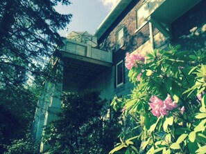 A building with a balcony, surrounded by greenery and pink flowers. - FULLY FURNISHED 1BR 1BA APT IN HISTORIC DOWNTOWN DISTRICT OF ASHEVILLE (Asheville)