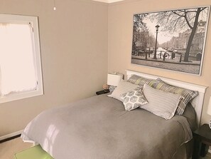 A bedroom with a bed, pillows, a nightstand, a window, and a wall-mounted picture. - FULLY FURNISHED 1BR 1BA APT IN HISTORIC DOWNTOWN DISTRICT OF ASHEVILLE (Asheville)