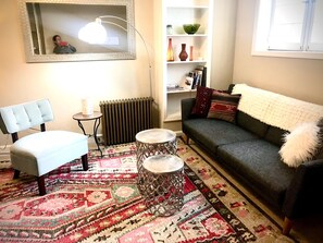 A living room with a sofa, a chair, a table, a radiator, and a bookshelf. - FULLY FURNISHED 1BR 1BA APT IN HISTORIC DOWNTOWN DISTRICT OF ASHEVILLE (Asheville)