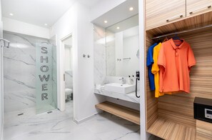 Ein modernes Badezimmer mit Duschbereich, Waschbecken und einem Holzwaschtisch mit hängender Kleidung.