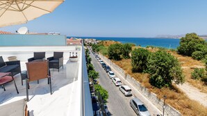 A rooftop terrace with outdoor seating, a view of the sea, and parked cars along the street. - Premium Suite with veranda and panoramic sea view, Notus Hotel Chania (Chania)