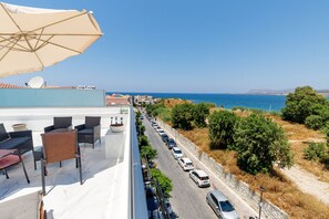 Eine Dachterrasse mit Sitzgelegenheiten im Freien, Blick auf das Meer und parkenden Autos an der Straße.