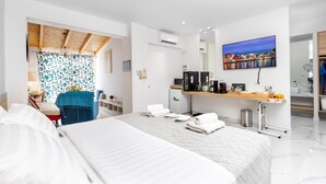 A modern hotel room with a large bed, a desk with a computer, a TV, and a cityscape view. - Premium Suite with veranda and panoramic sea view, Notus Hotel Chania (Chania)