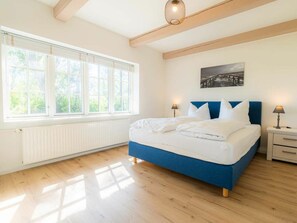 A bedroom with a large bed, two bedside tables, a window with blinds, a radiator, and a ceiling light fixture. - Holiday Apartment 3 "norderoog" (Tating)