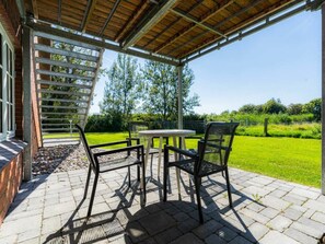 An outdoor patio with a table and chairs, a pergola, and a view of a green landscape. - Holiday Apartment 3 "norderoog" (Tating)
