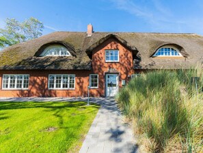 A traditional brick building with a thatched roof, a central door, and a small attached structure. - Holiday Apartment 3 "norderoog" (Tating)