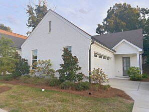 Einbungalow mit weißer Fassade, einer Garagentür und einem Vorgarten mit verschiedenen Sträuchern und einem kleinen Baum.