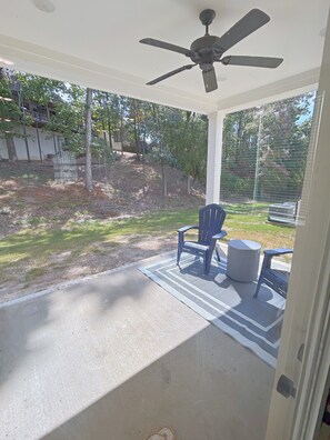 Un patio techado con ventilador de techo, una mesa con sillas y vista a un jardín.