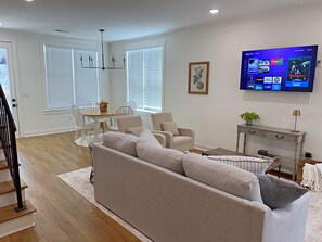 Ein modernes Wohnzimmer mit einer Couch, einem Esstisch, Stühlen und einem an der Wand befestigten Flachbildfernseher.