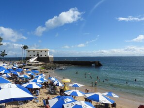 A beach with multiple umbrellas, a building, and the ocean. - Studio Ondina: Air conditioning, Wi-Fi, and parking near Barra. (Salvador)