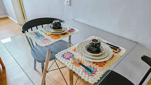 Una mesa de comedor con dos sillas, una cafetera y un plato sobre un mantel.