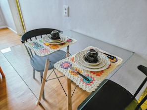 Una mesa de comedor con dos sillas, una cafetera y un plato sobre un mantel.