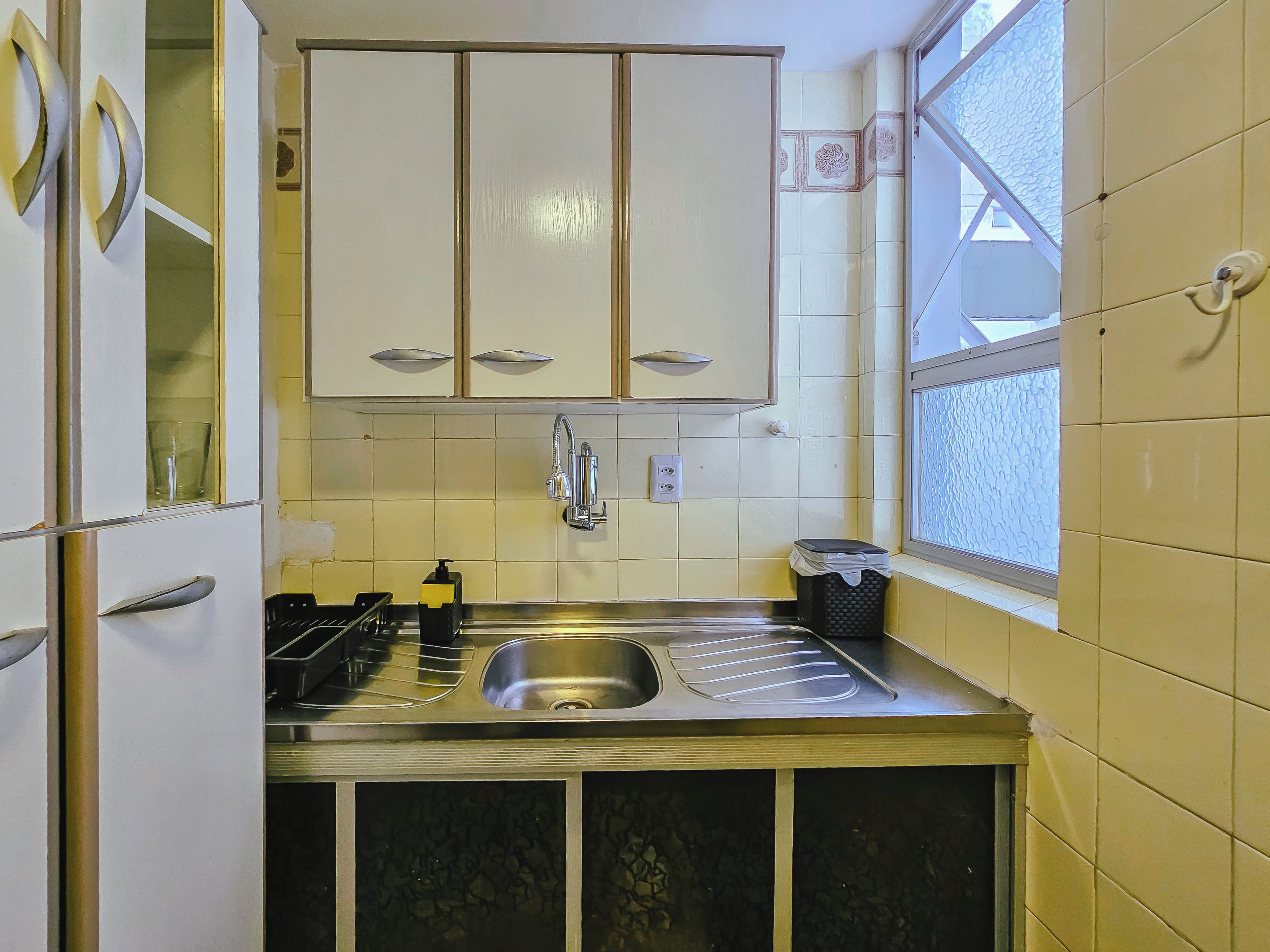 A compact kitchen with a double sink, a window, and cabinets above the countertop.