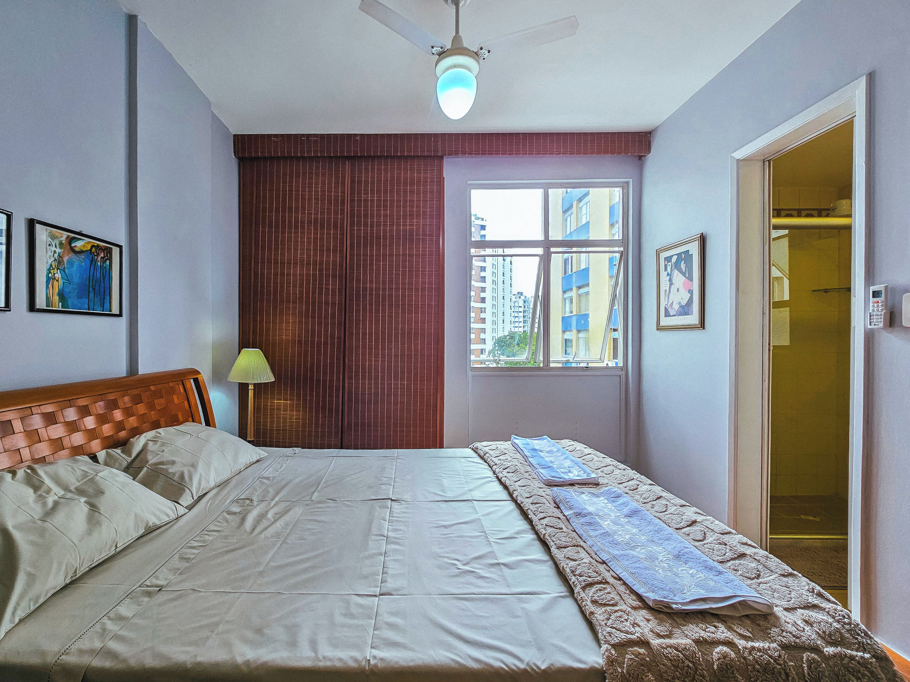 Un dormitorio con cama, ventana, puerta y ventilador de techo.