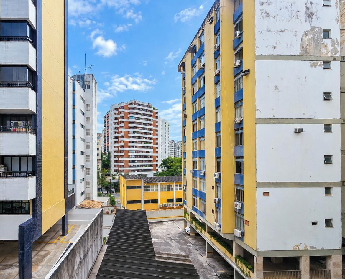 A multi-story residential building with balconies, a central staircase, and a clear sky.
