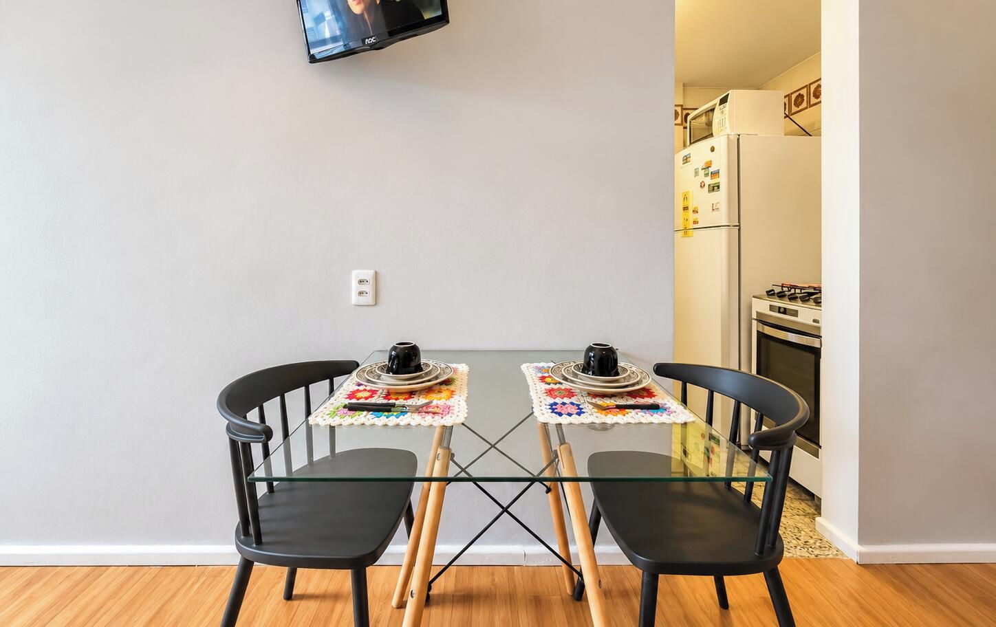 A small dining area with a glass table, two chairs, and a television mounted on the wall.