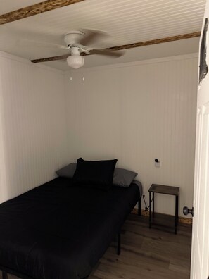 Ein Schlafzimmer mit einem Bett, einem Nachttischchen, einem Deckenventilator und einer Holzbalkendecke.