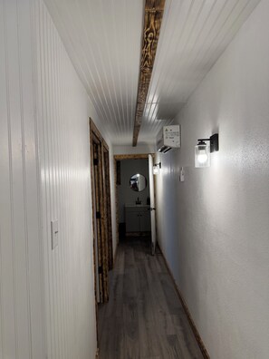 Ein Flur mit weißen Wänden, Holzbodenverkleidung an der Decke und einem Badezimmer im Hintergrund.