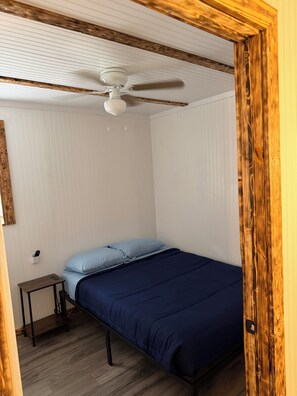 A bedroom with a bed, a nightstand, a ceiling fan, and wooden paneling. - The Blondell : Cozy 2BR Country Escape Near Lake Fork (Quitman)