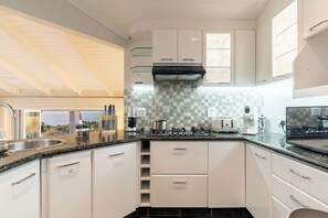 A modern kitchen with white cabinets, a black countertop, and a view of the ocean. - Camps Bay Fam Villa, Pool, Hot Tub - Bella Riposa (Cape Town)