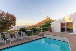 A swimming pool with lounge chairs, a view of a mountain, and a building with a glass door. - Camps Bay Fam Villa, Pool, Hot Tub - Bella Riposa (Cape Town)