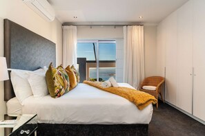 A hotel room with a large bed, a view of the sea, a chair, and a wardrobe. - Camps Bay Fam Villa, Pool, Hot Tub - Bella Riposa (Cape Town)