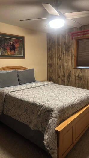 Ein Schlafzimmer mit einem Bett, einem Deckenventilator, einem Fenster mit Jalousien und einem Wandbild.