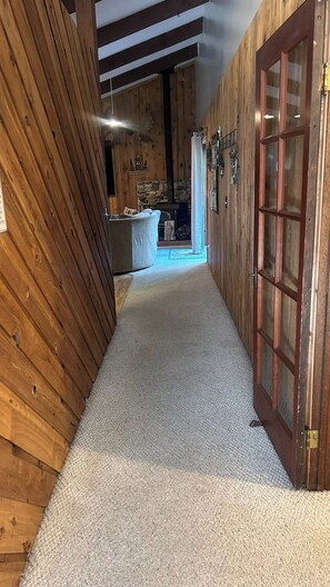 Ein schmaler Korridor mit Holzwänden und Teppichboden, der zu einem Raum mit Kamin aus Stein führt.