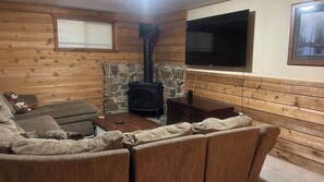 A cozy living room with a stone fireplace, a television, and a sofa. - 6 Bedroom Downtown Lodge w/ Game Room, BBQ, Deck (Gold Coast)
