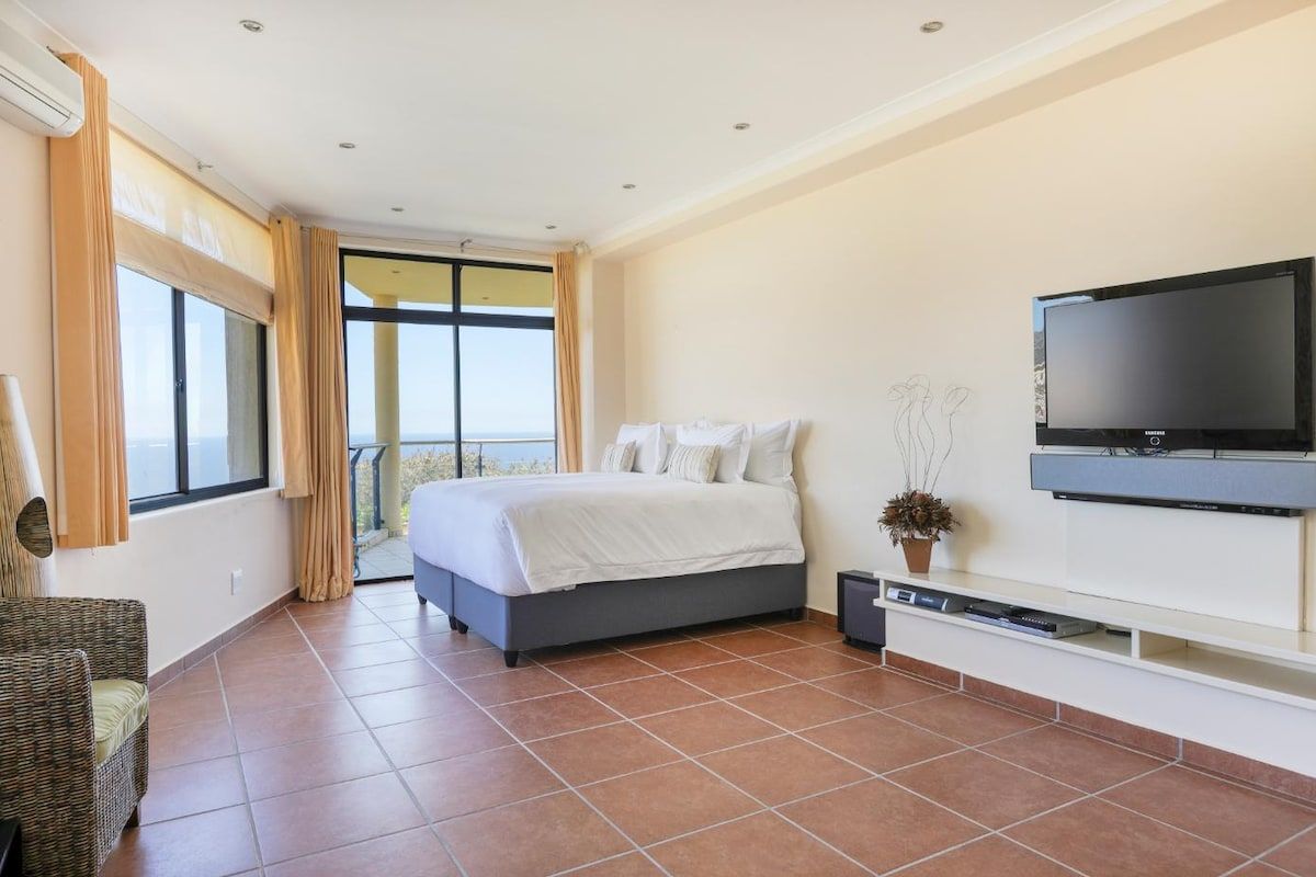 A modern bedroom with a large bed, a television, and a balcony view.