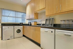 A kitchen with wooden cabinets, a washing machine, a dishwasher, and a coffee maker. - Walking distance to Camps Bay Beach, Views - Merridew (Cape Town)