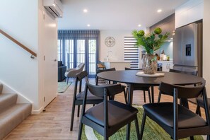 A modern kitchen with a built-in refrigerator, a dining area with a round table and chairs, and a staircase leading to another level. - Peaceful 4BR Townhouse - Near Avon River + Garage (Christchurch)
