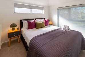A bedroom with a bed, pillows, a nightstand, a lamp, and a window. - Peaceful 4BR Townhouse - Near Avon River + Garage (Christchurch)