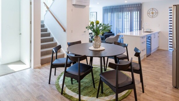 Een moderne keuken met een inbouwoven, een eethoek met een ronde tafel en stoelen, en een trap naar een verdieping.