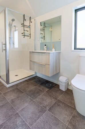 A bathroom with a glass shower enclosure, a white toilet, and a vanity with a mirror. - Peaceful 4BR Townhouse - Near Avon River + Garage (Christchurch)