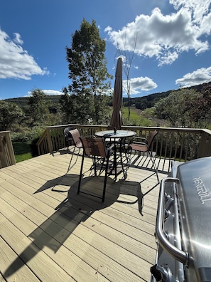 A deck with a table and chairs, a grill, and a view of a green landscape.
