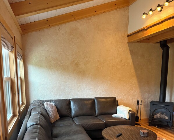 A cozy living room with a leather sofa, a round coffee table, and a wood-burning stove.