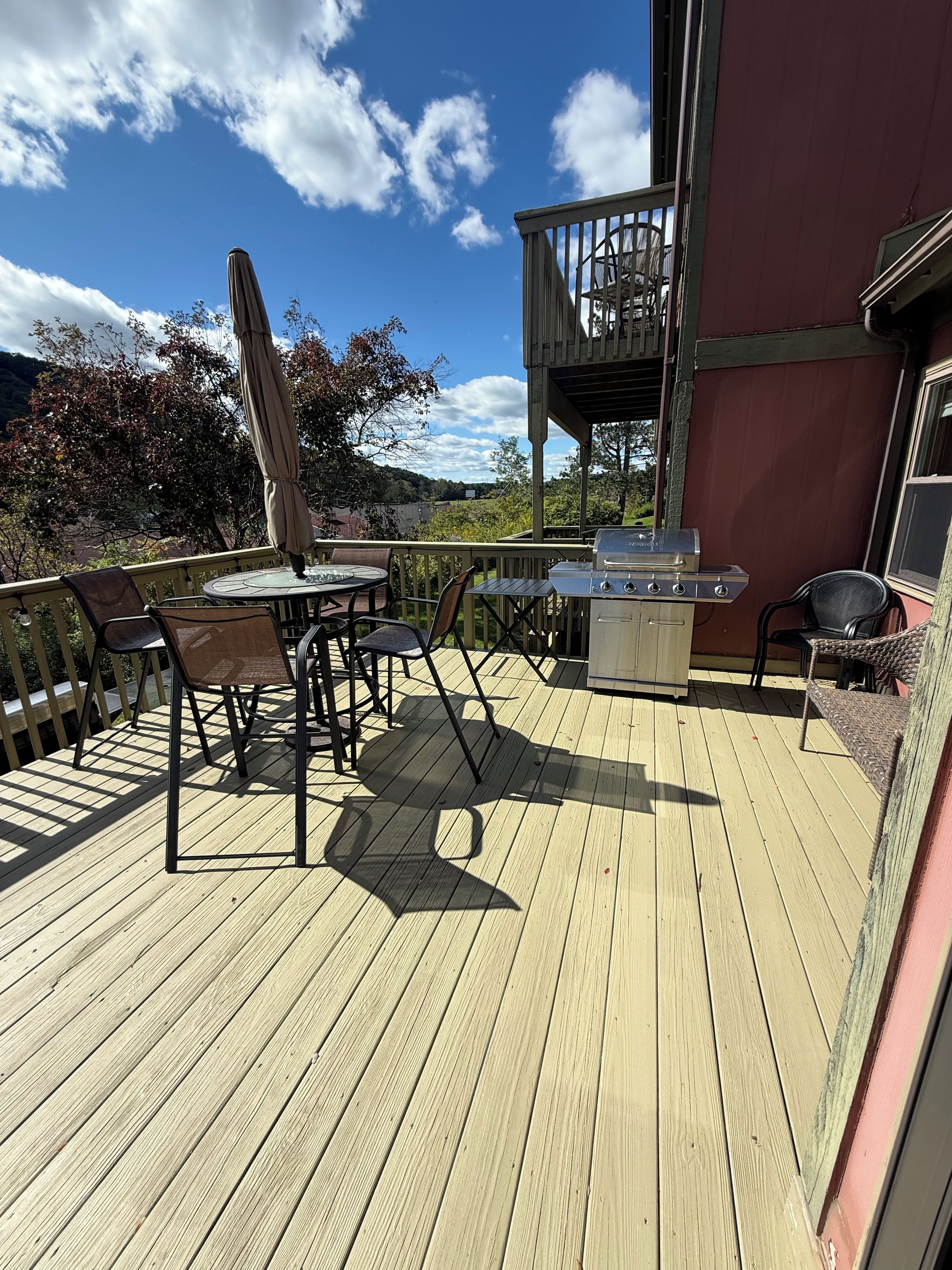 A wooden deck with outdoor furniture, a grill, and a view of the surrounding landscape.