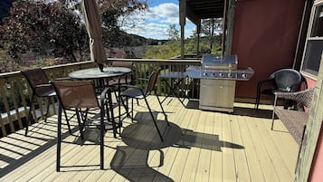 A wooden deck with outdoor furniture, a grill, and a view of the surrounding landscape.