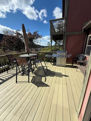 A wooden deck with outdoor furniture, a grill, and a view of the surrounding landscape.